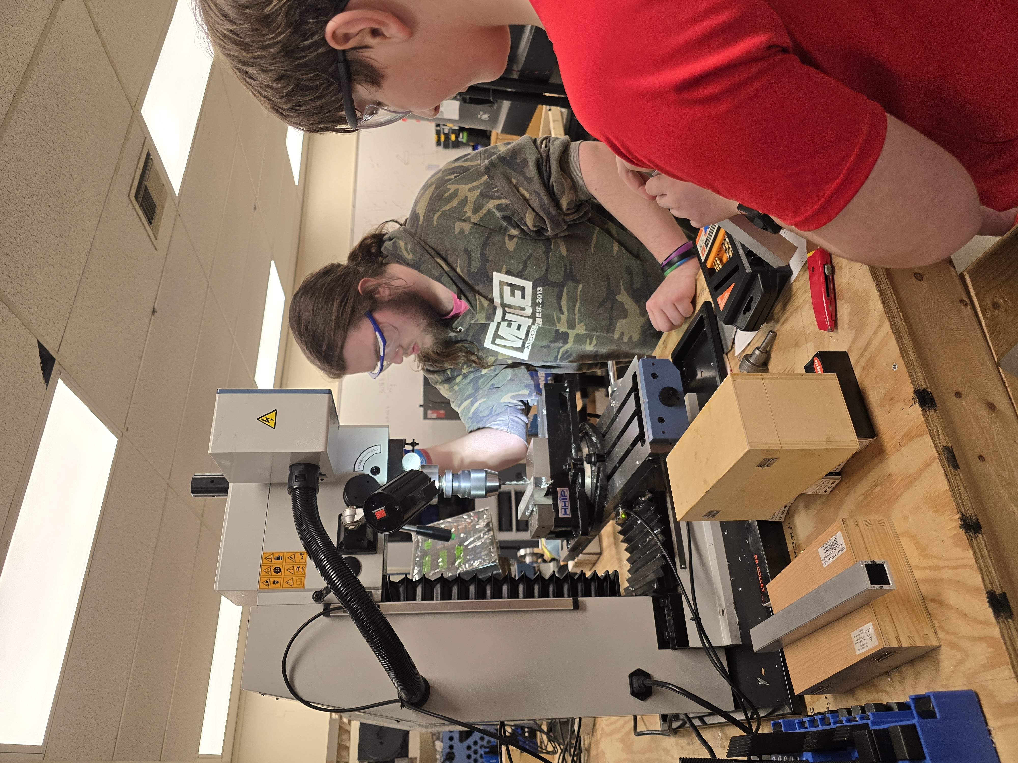 A RoboRam student teaches another how to use benchtop mill.